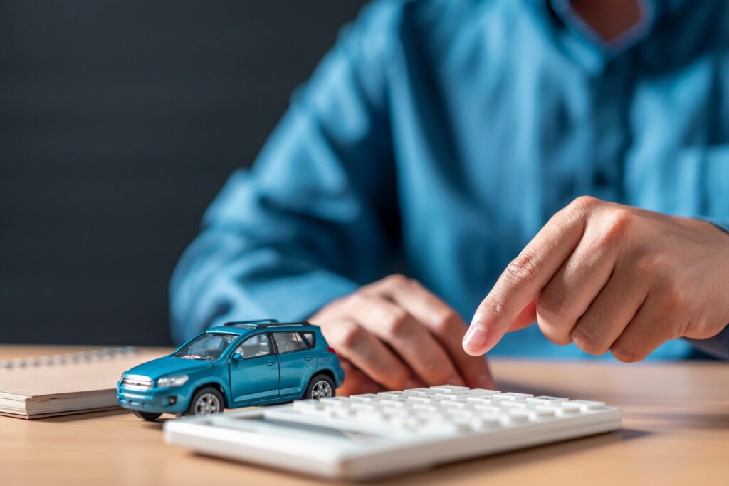 A man is pointing at a blue car on a calculator.